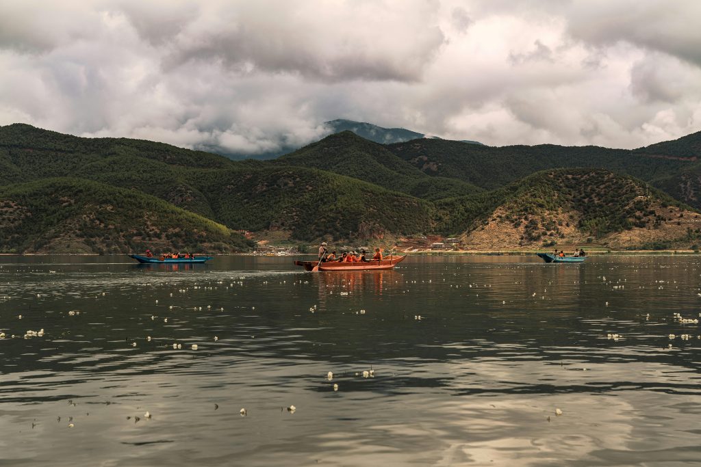 Colorful boats on a tranquil lake surrounded by lush mountains under cloudy skies.