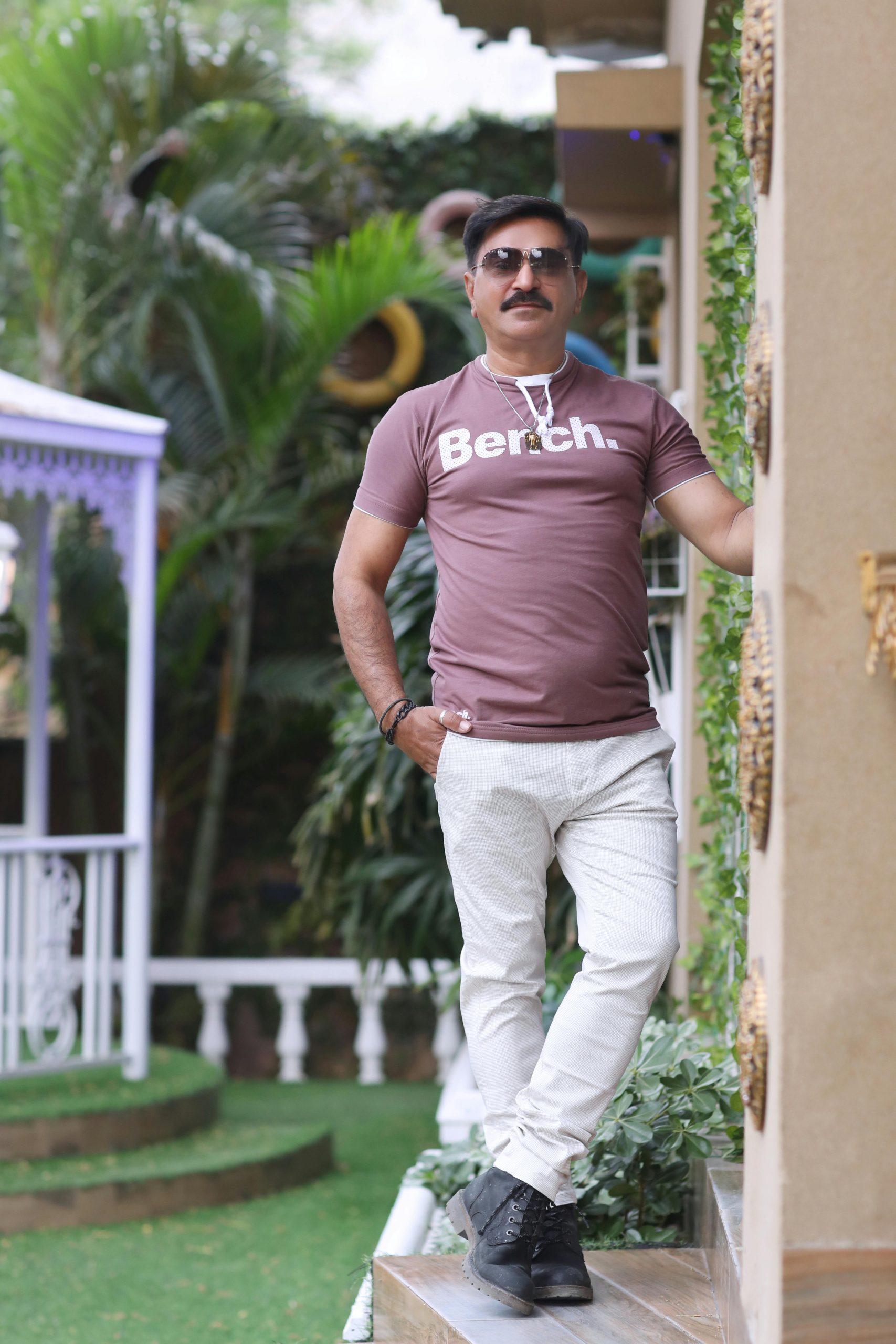 Elegant man in sunglasses posing outdoors by a column, wearing casual t-shirt and pants.